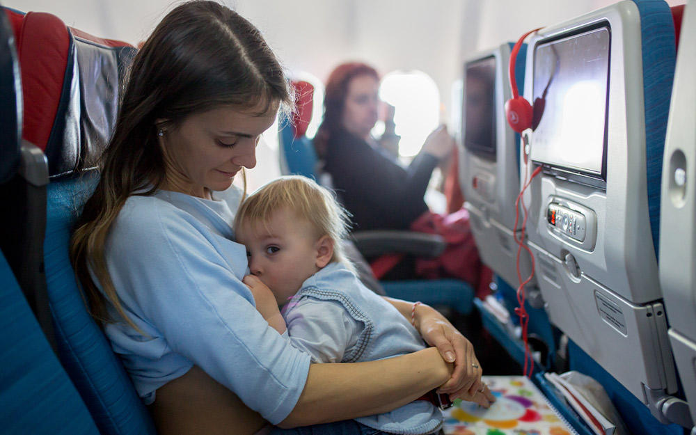Mutter sitzt mit zufrieden nuckelndem Kind im Flugzeug